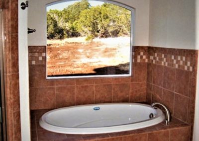 White garden tub with rust colored wall tile and clear glass arched picture window