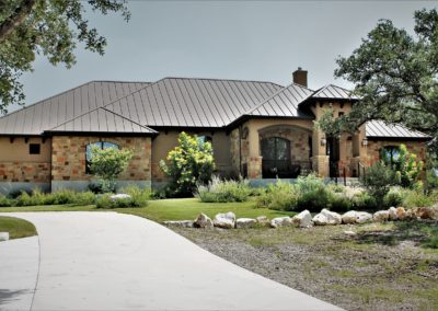 Large home exterior with tan stucco and brown rock and metal roof