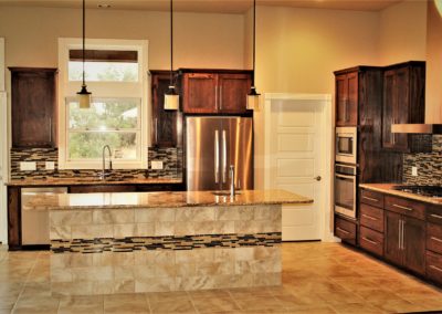 Dark Oak Cabinets with chrome hardware and kitchen island with granite countertop and glass tile backsplash