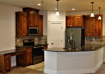 Kitchen with Built-In Desk. Dark alder kitchen cabinets with black countertops and bar wall pendant lighting
