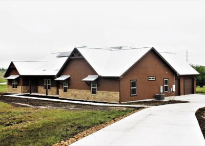 Texas Farmhouse. Brown stucco with tan rock wainscoat and silver standing seam metal roof