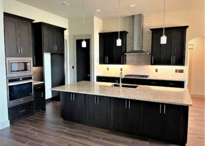 custom alder cabinets with dark stain and large kitchen island with granite countertops. Tile backsplash.