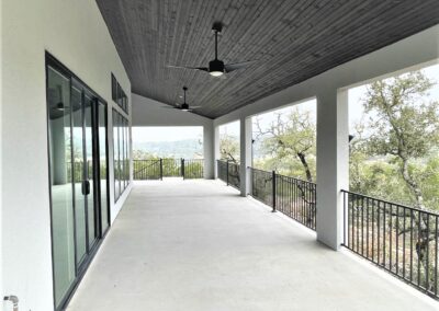 large covered patio with dark walnut wood ceiling, white stucco walls and black wrought iron railing