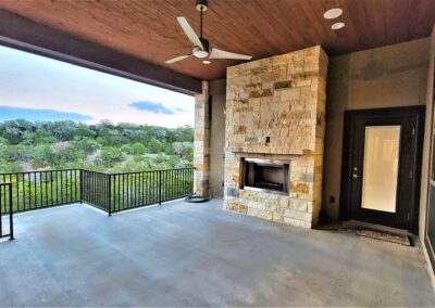 Fireplace on covered patio with wood ceiling and wrought iron railing.